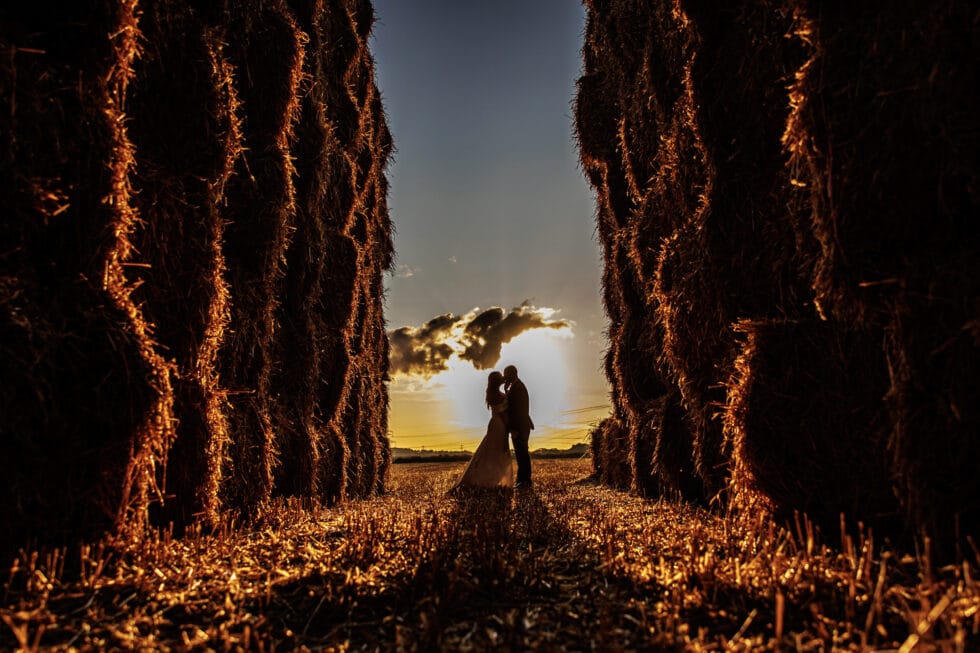 couple standing in between haystacks at sunset